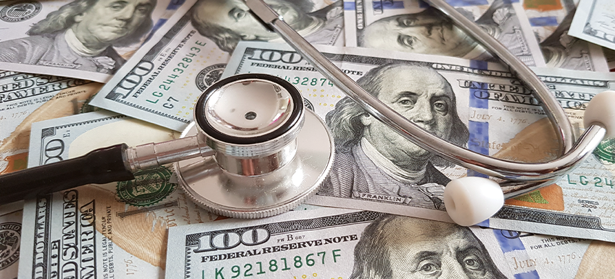 Stethoscope lies on a large pile of one-hundred-dollar bills
